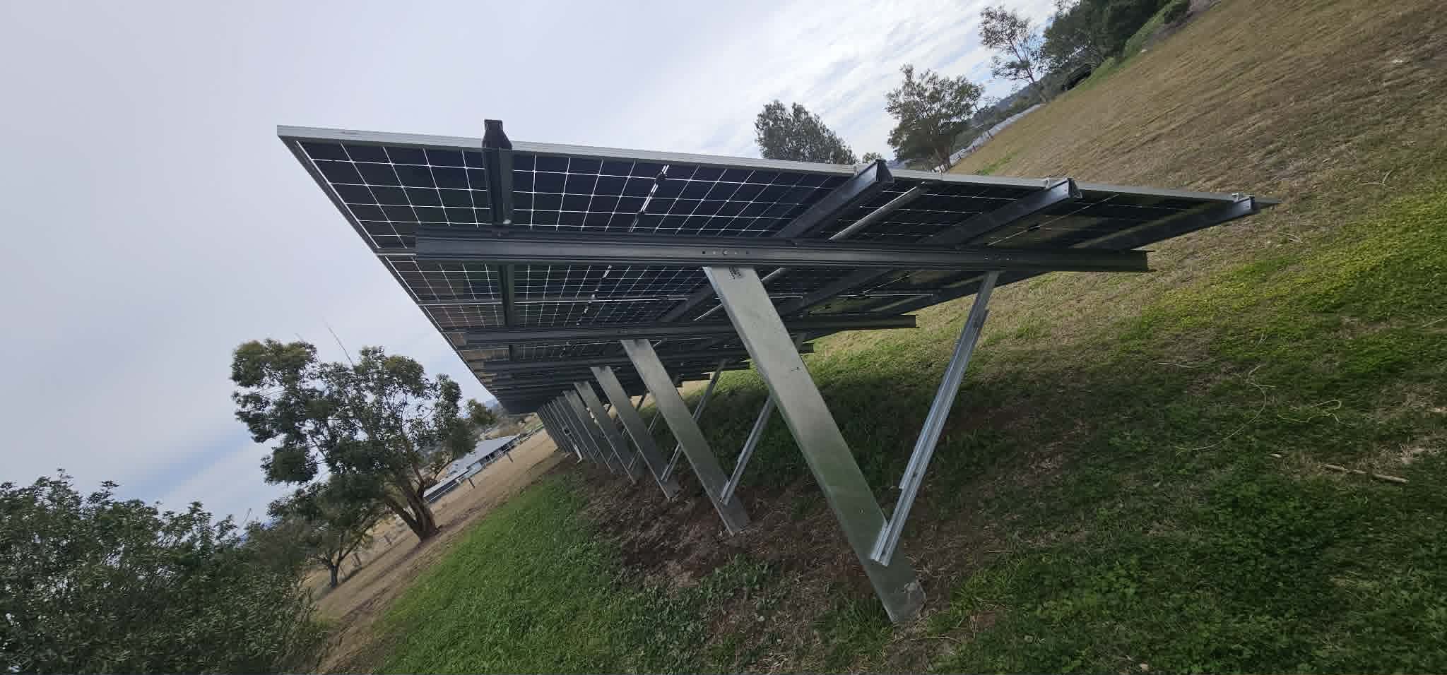 Solar panels on galvanised tilt frames set into a grassy hillside in rural Queensland