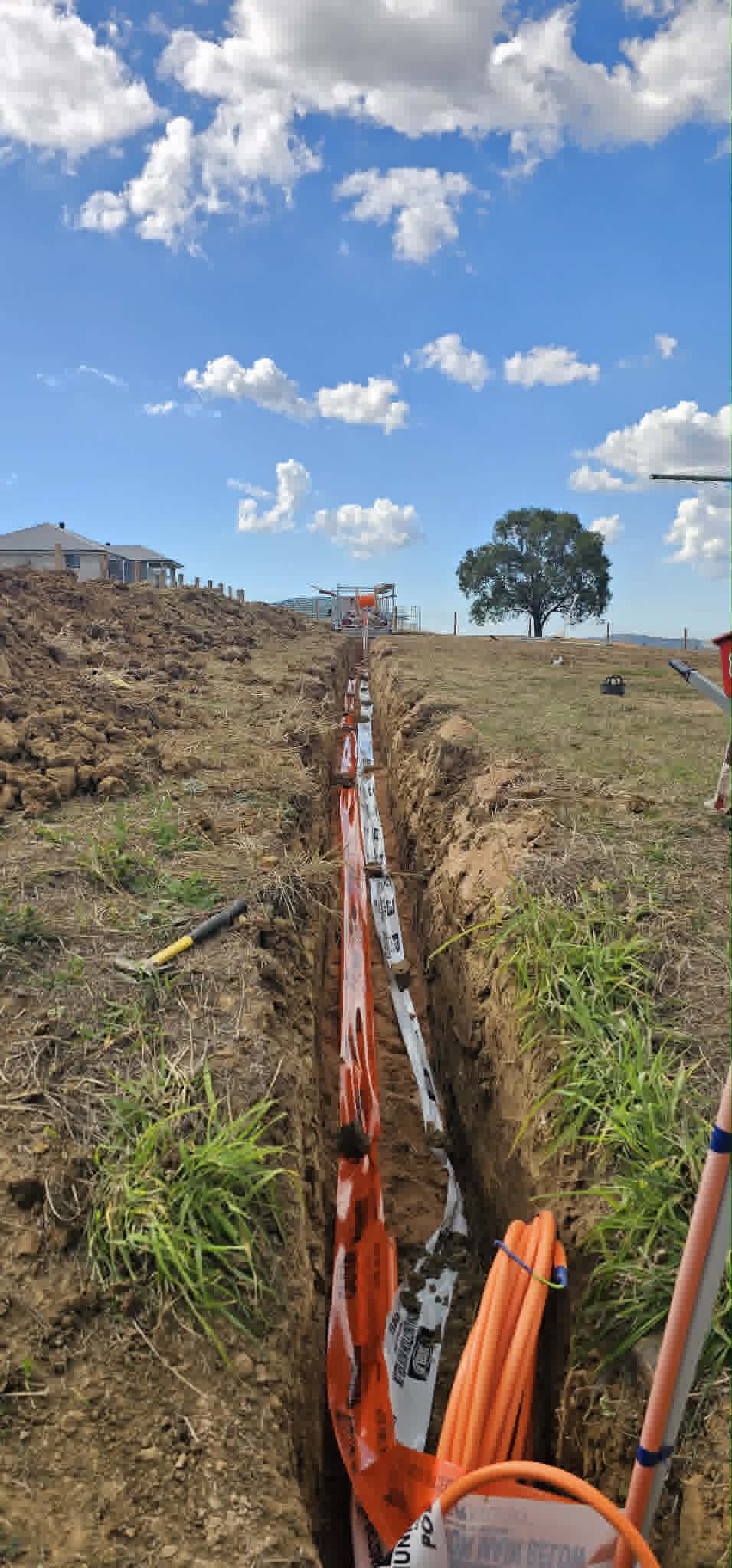 Long trench across a rural block with orange electrical conduit laid in the bottom